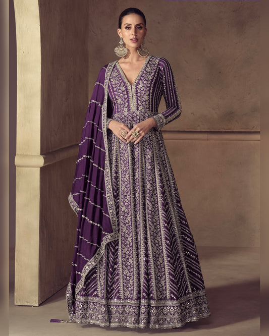 Woman wearing a purple and white embroidered traditional outfit against a neutral background