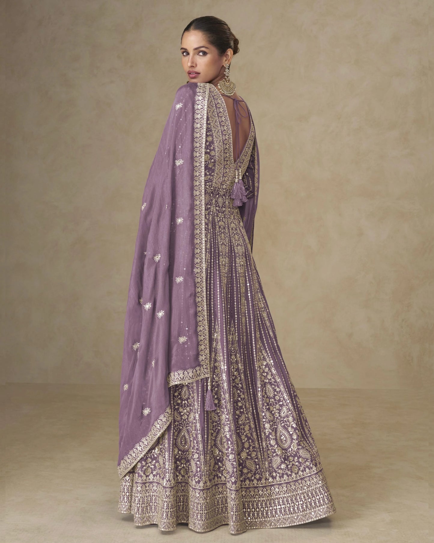 Woman wearing a traditional outfit with a purple dupatta against a beige background