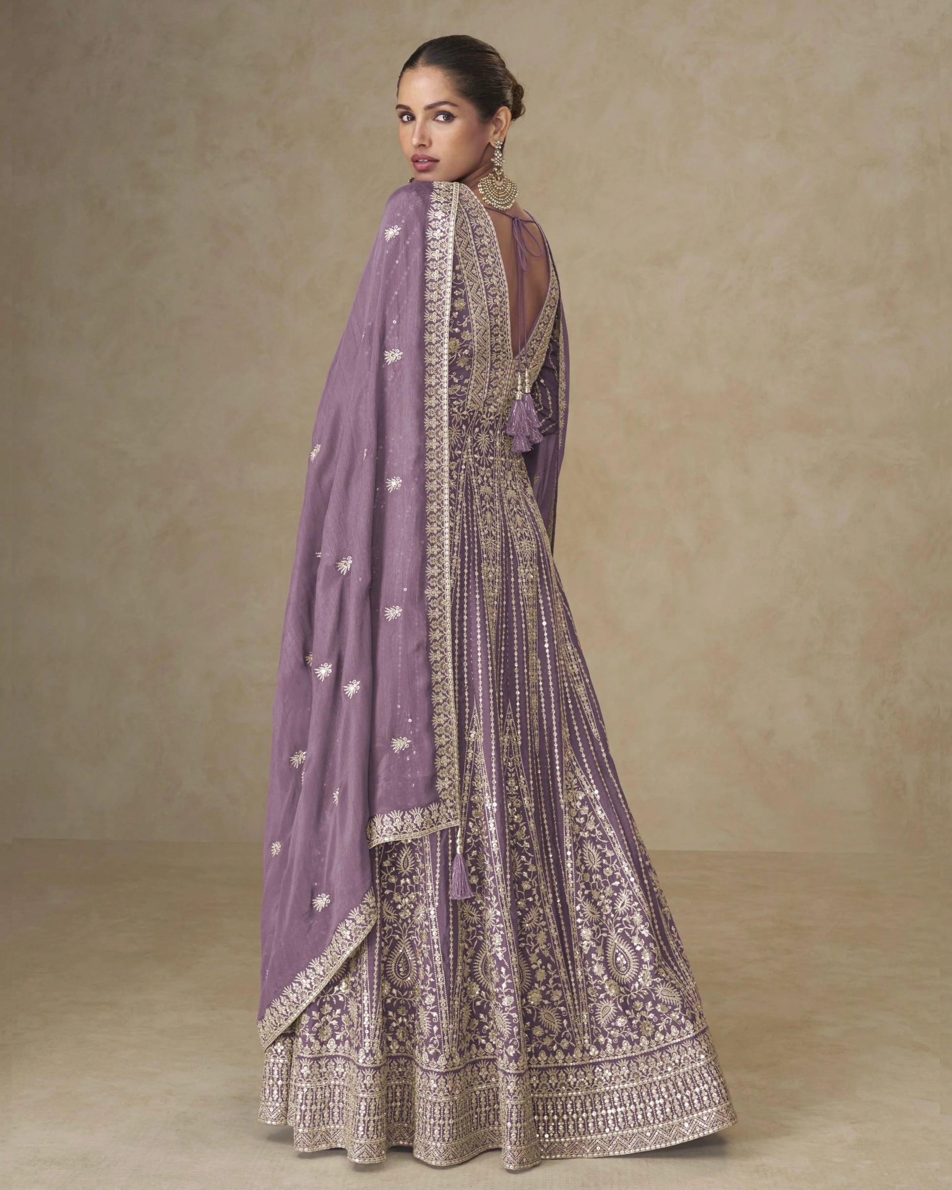 Woman wearing a traditional outfit with a purple dupatta against a beige background
