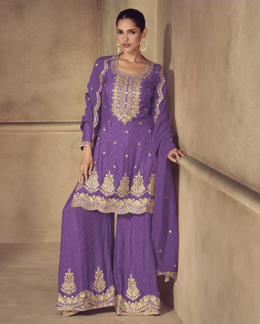 Woman wearing a purple embroidered traditional outfit against a beige wall.