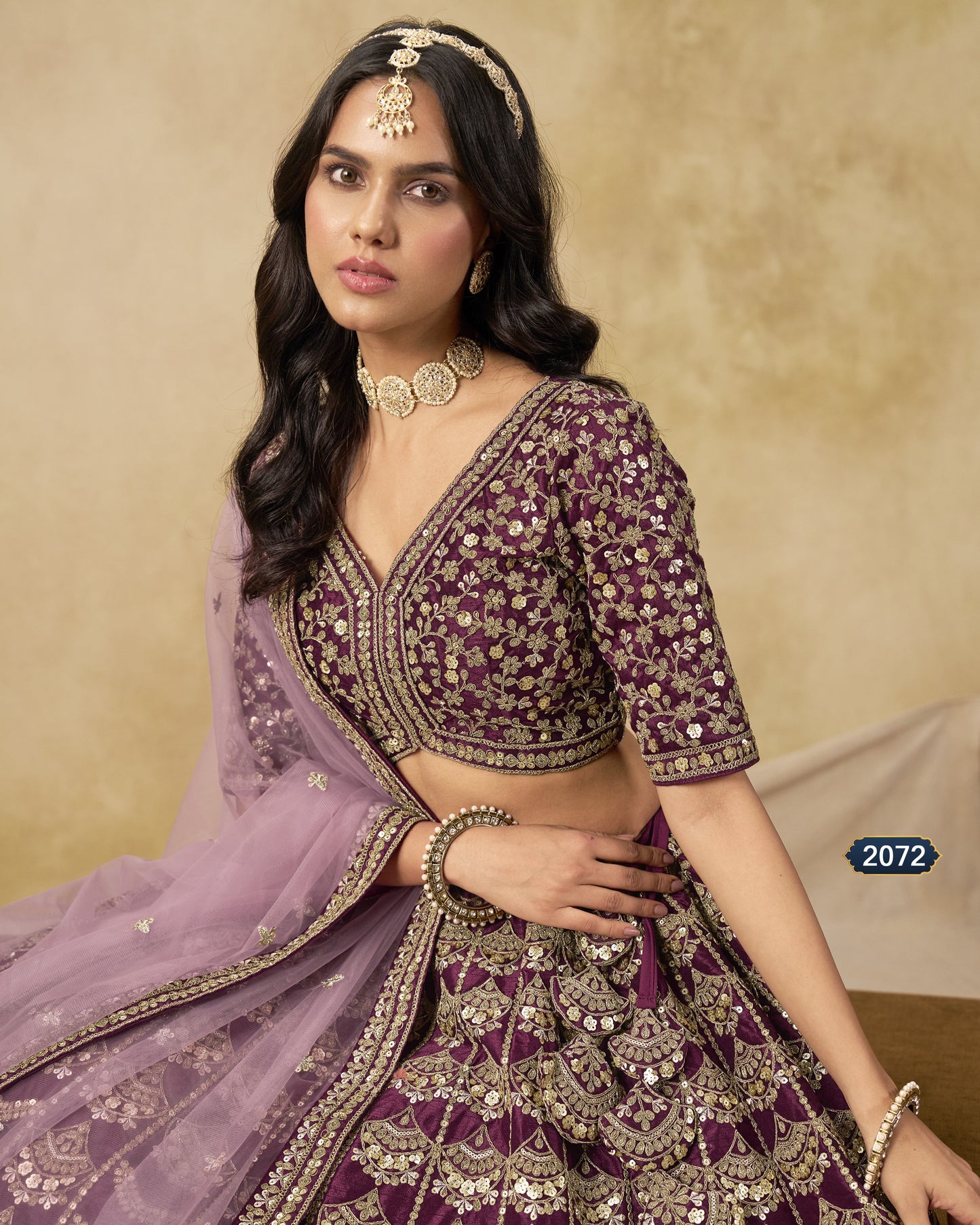 Woman in a traditional embroidered outfit with a purple dupatta against a beige background