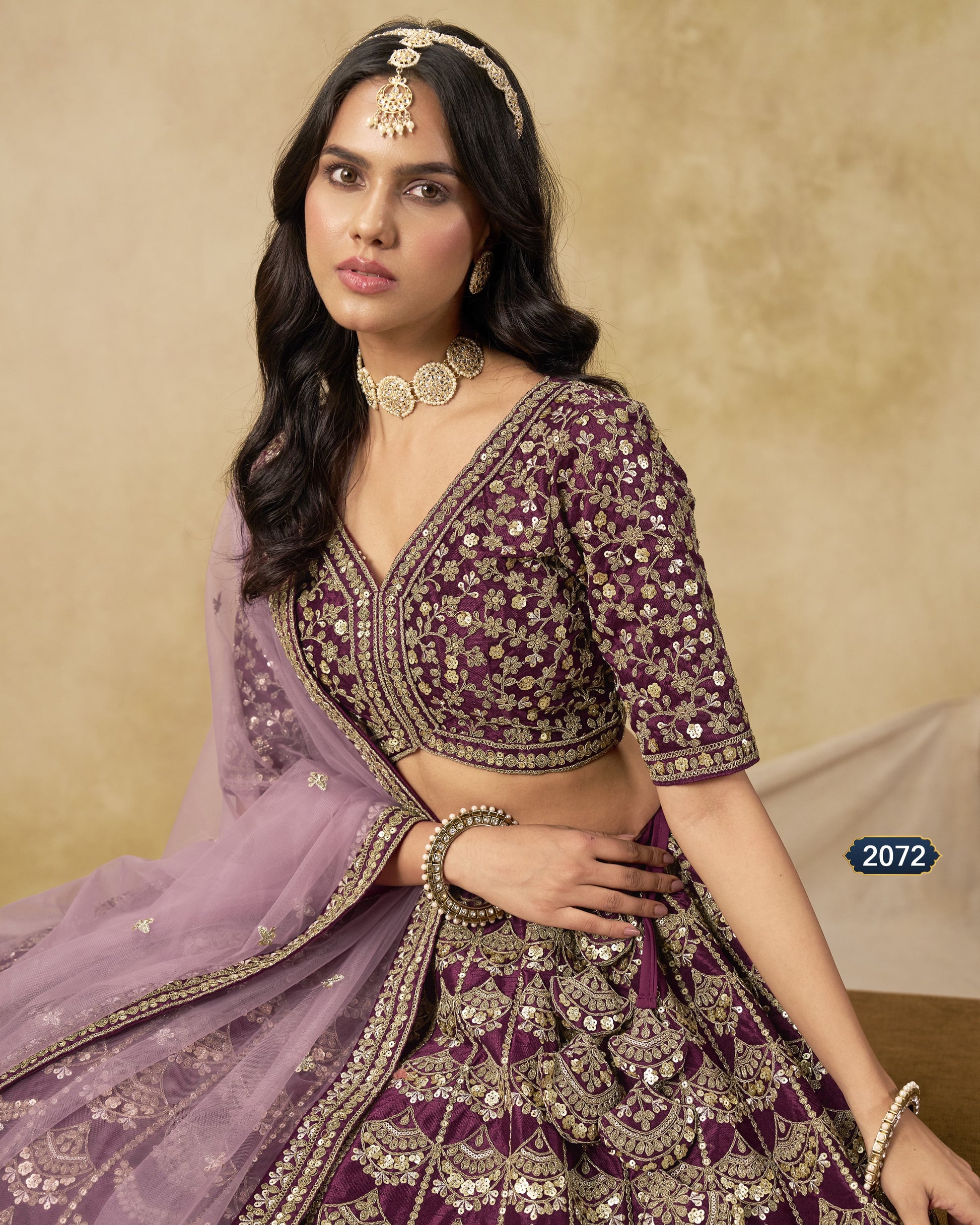 Woman in a traditional embroidered outfit with a purple dupatta against a beige background