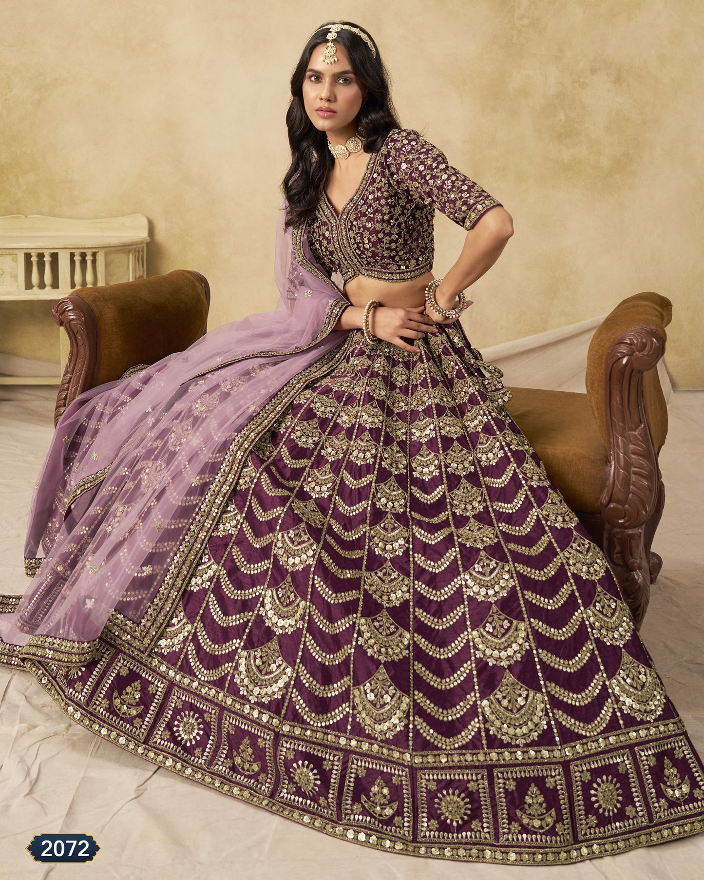 Woman in a traditional purple and gold embroidered outfit sitting on a wooden chair.