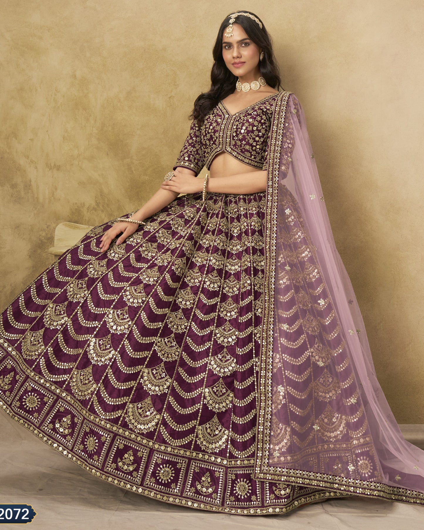 Woman wearing a traditional purple and gold embroidered lehenga with a beige background