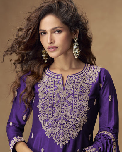 Woman wearing a purple embroidered outfit with gold jewelry against a brown background