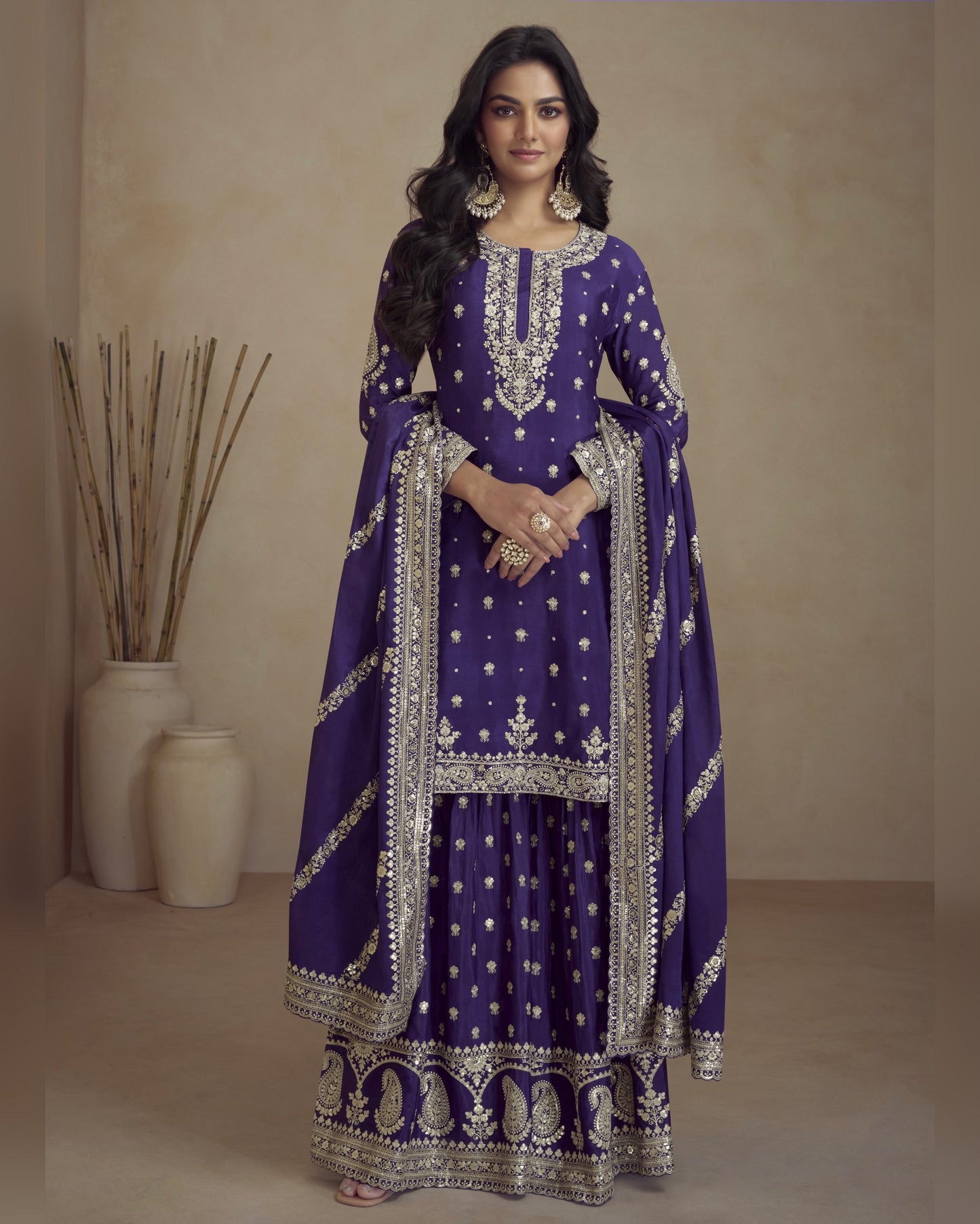 Woman wearing a purple embroidered traditional outfit with silver details against a beige background.