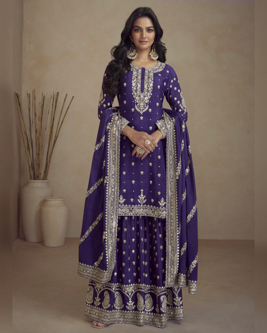 Woman wearing a purple embroidered traditional outfit with silver details against a beige background.