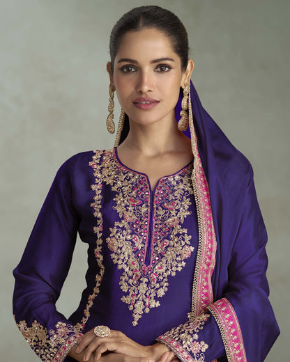 Woman wearing a purple embroidered traditional outfit with a plain background