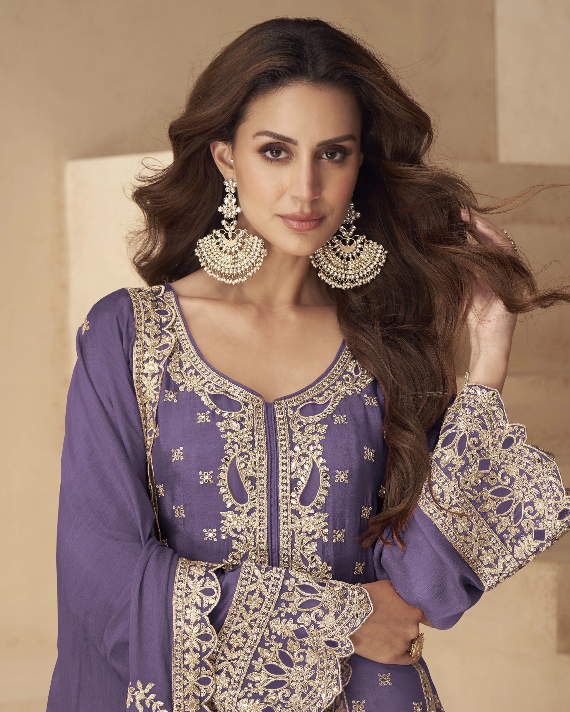 Woman wearing a purple and gold embroidered outfit with jewelry against a beige background