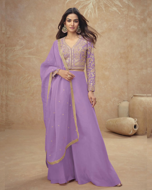 Woman wearing a purple saree with gold accents against a beige background