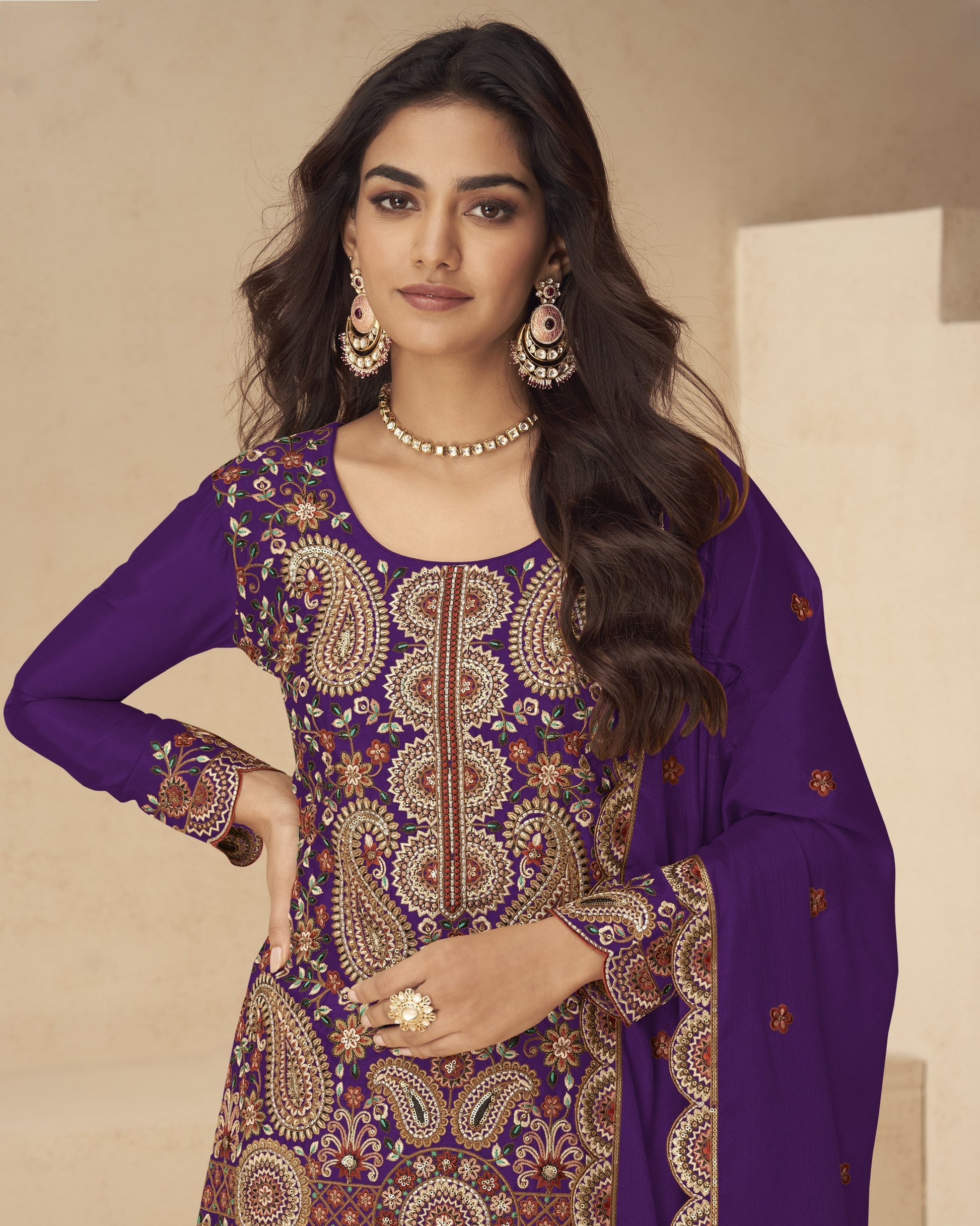 Woman wearing a purple embroidered traditional outfit with gold jewelry against a beige background