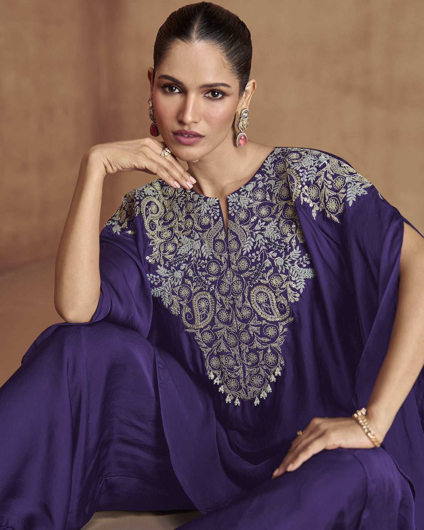 Woman wearing a purple traditional outfit with intricate embroidery on a beige background