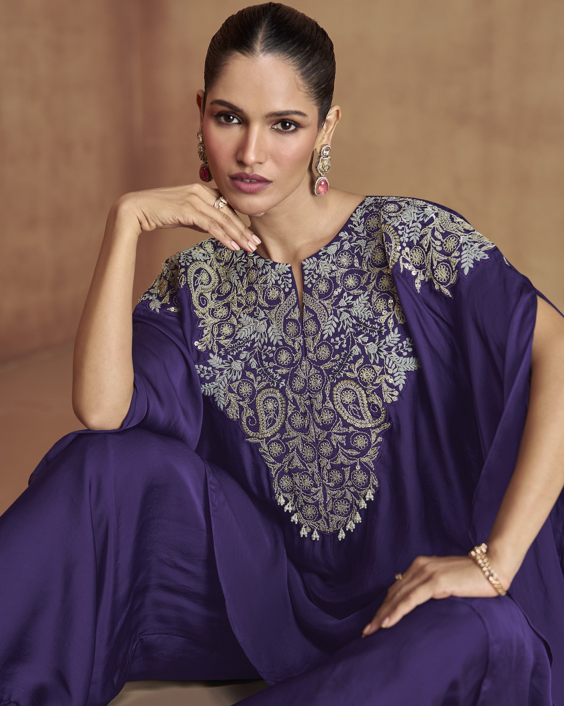 Woman wearing a purple traditional outfit with intricate embroidery on a beige background