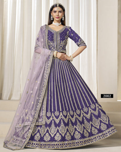 Woman wearing a purple and gray embroidered traditional outfit with a sheer dupatta against a white curtain background.