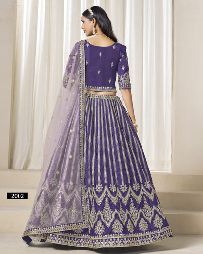Woman wearing a purple embroidered traditional outfit with a sheer dupatta against a white curtain background.