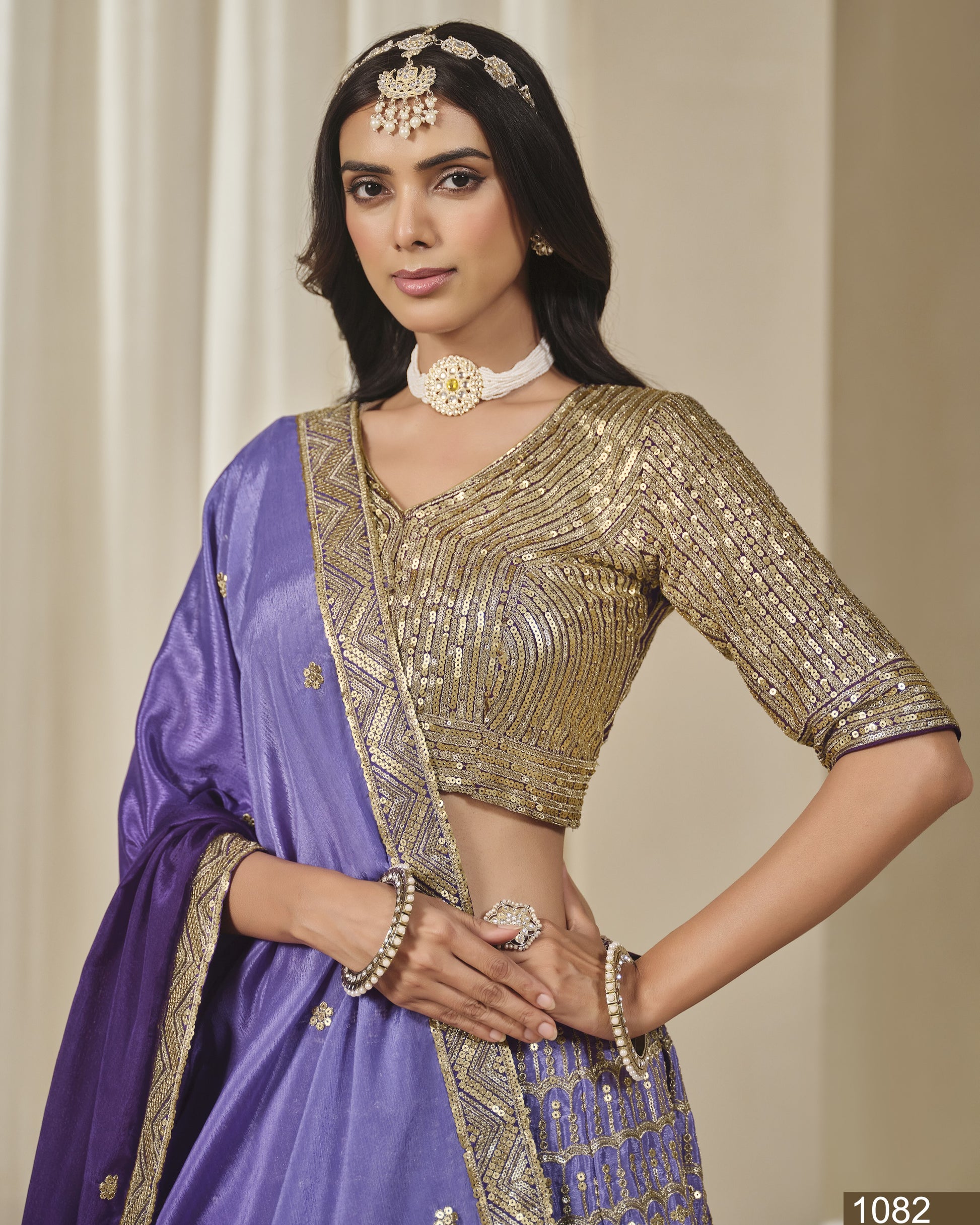 Woman wearing a traditional outfit with a gold blouse and purple saree against a neutral background
