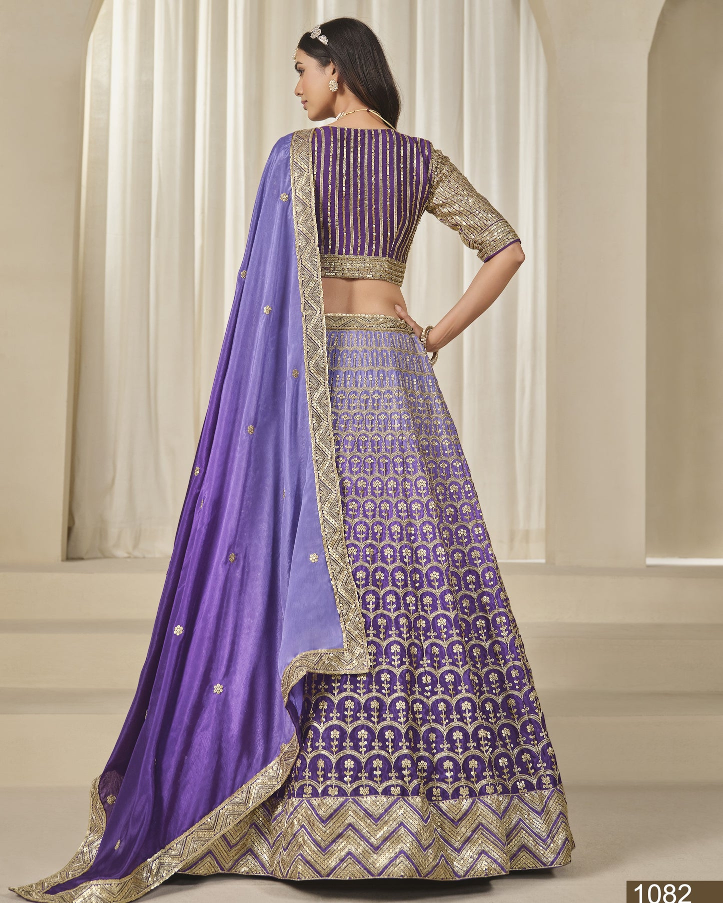 Woman wearing a purple and gold traditional outfit with a matching dupatta in an indoor setting.