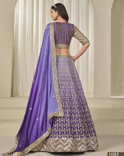 Woman wearing a purple and gold traditional outfit with a matching dupatta in an indoor setting.