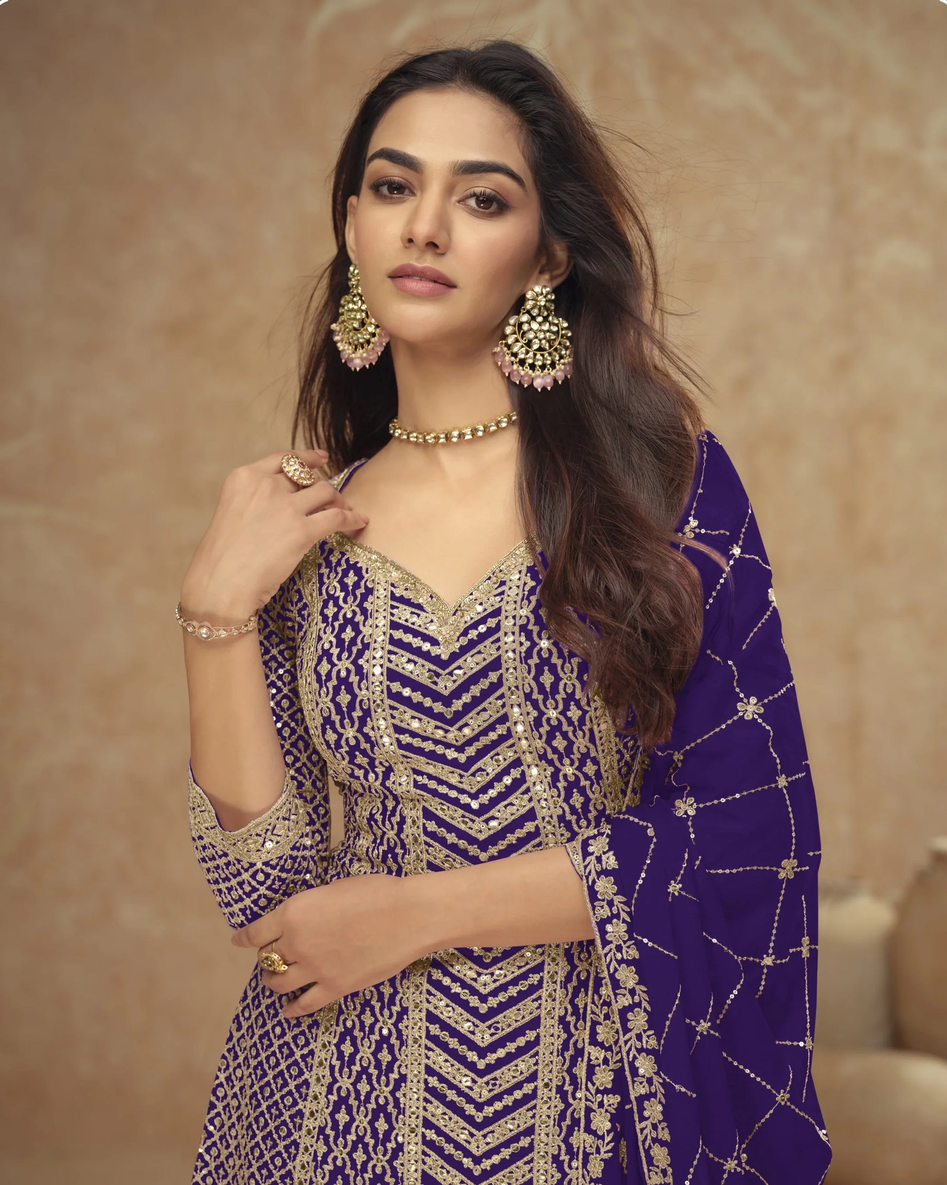 Woman in a purple and gold traditional outfit with jewelry against a beige background
