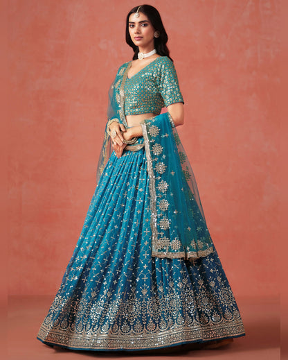 Woman wearing a blue embroidered lehenga with a matching blouse against a pinkish-brown background