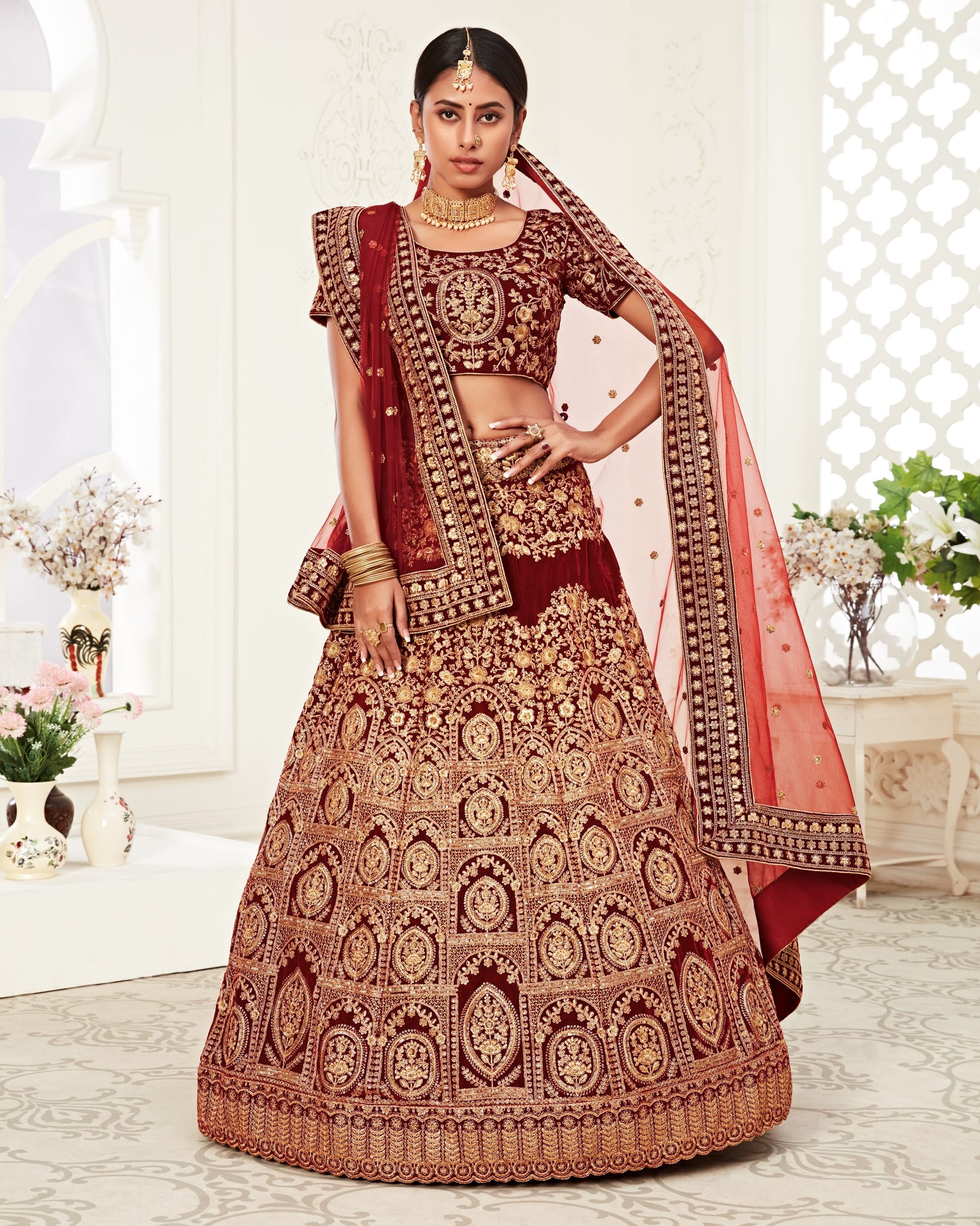 Woman in traditional embroidered red and gold lehenga with a white background