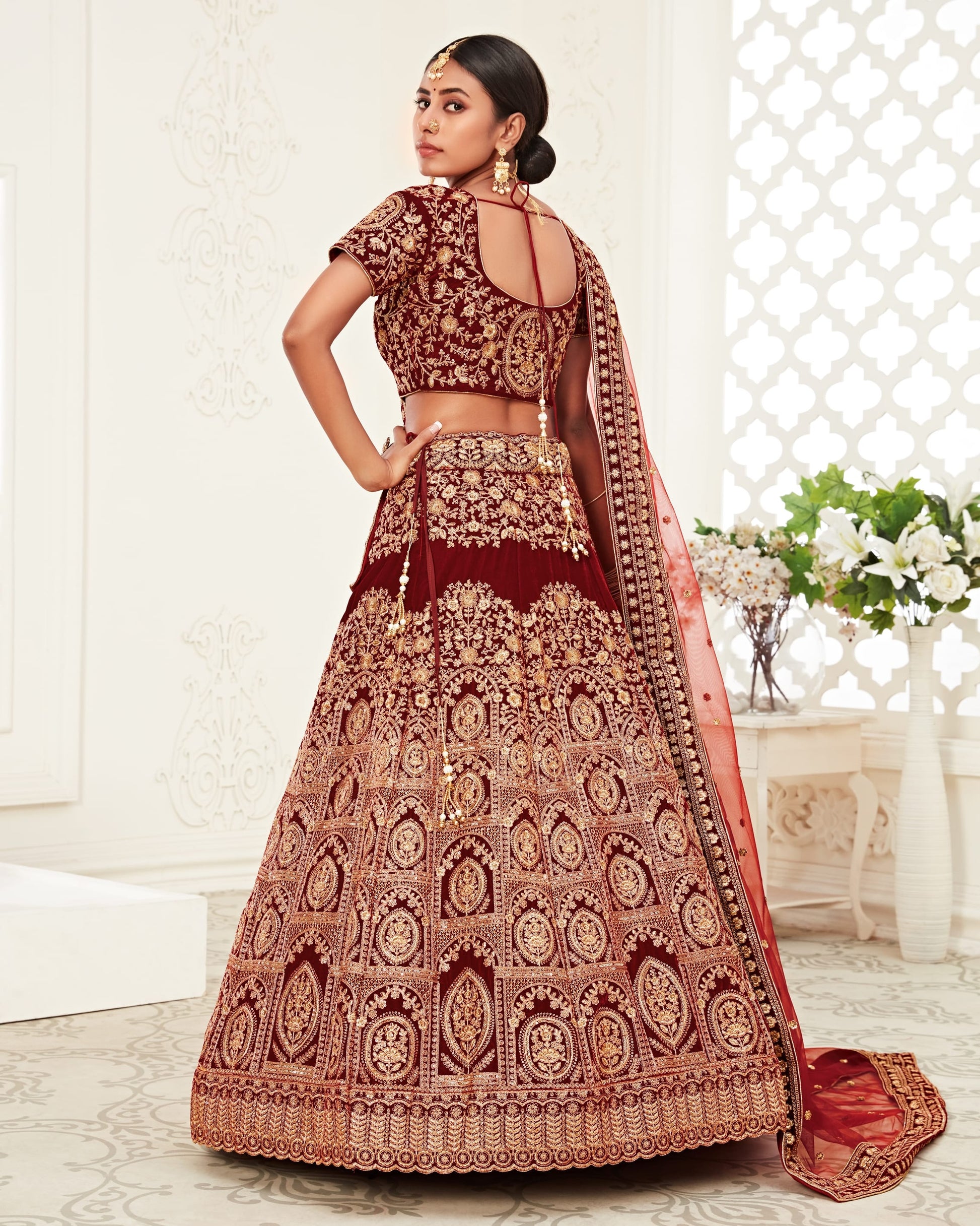 Woman wearing a traditional maroon and gold embroidered lehenga in an indoor setting.
