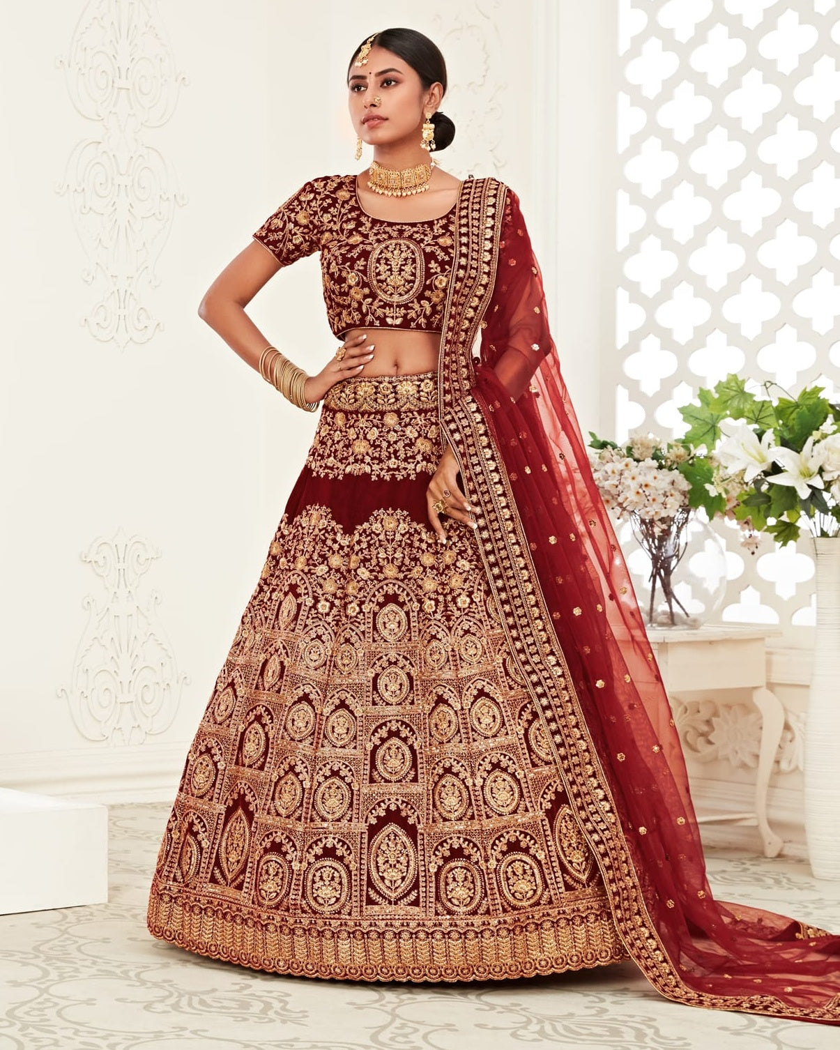 Woman wearing a maroon and gold embroidered traditional outfit in a bright room.