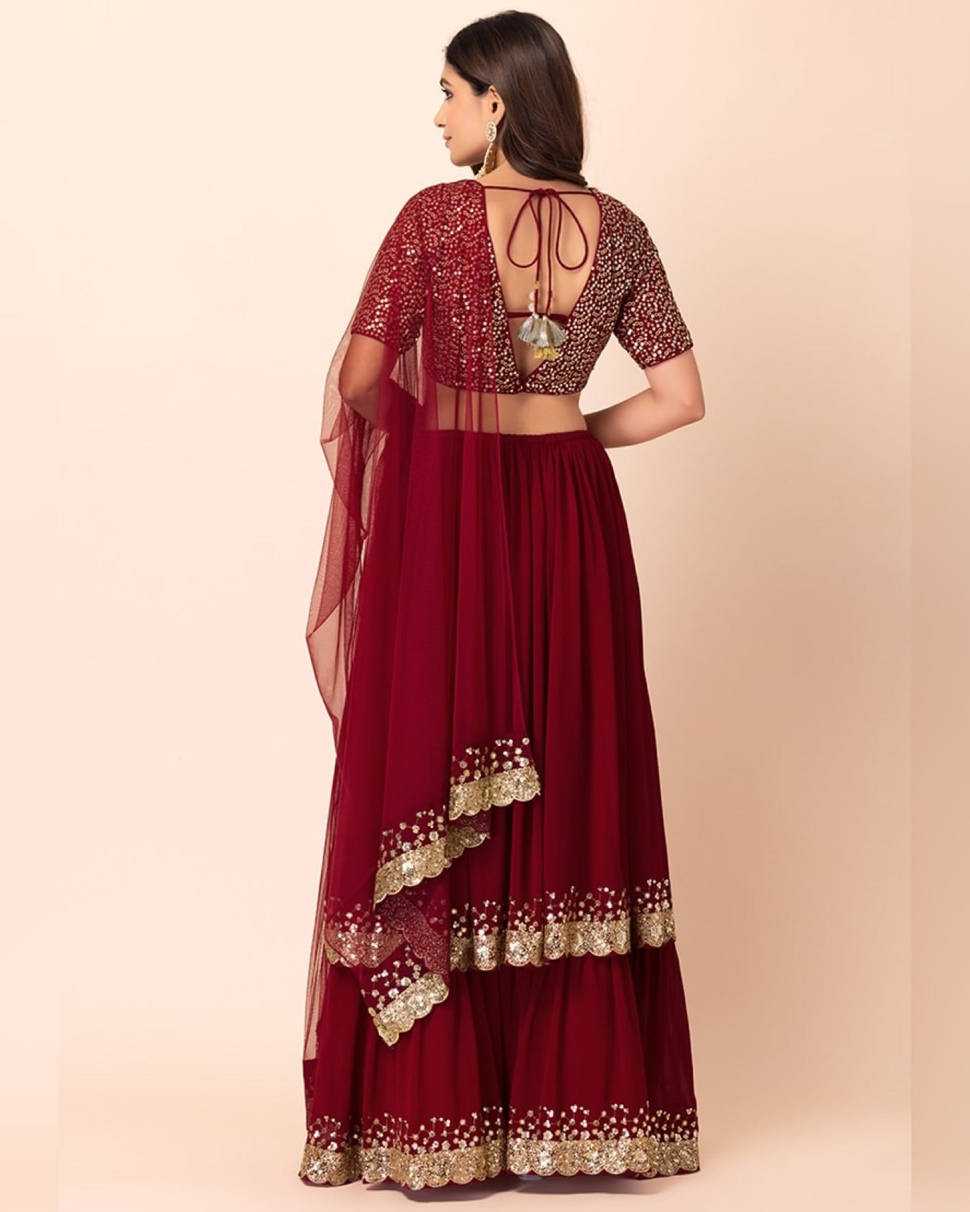 Maroon traditional outfit with gold embroidery on a beige background