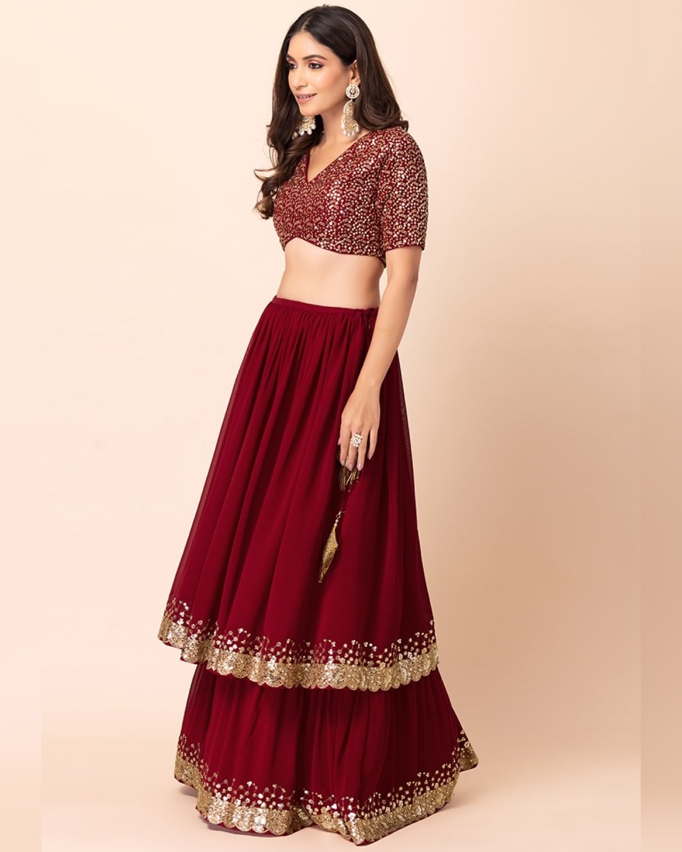 Woman wearing a maroon traditional outfit with gold embroidery on a beige background