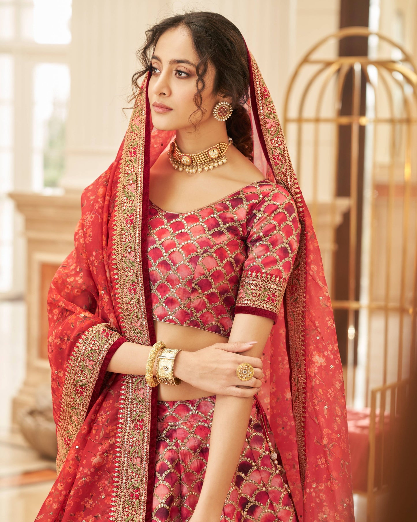 Woman in traditional red and gold outfit with jewelry in an elegant indoor setting