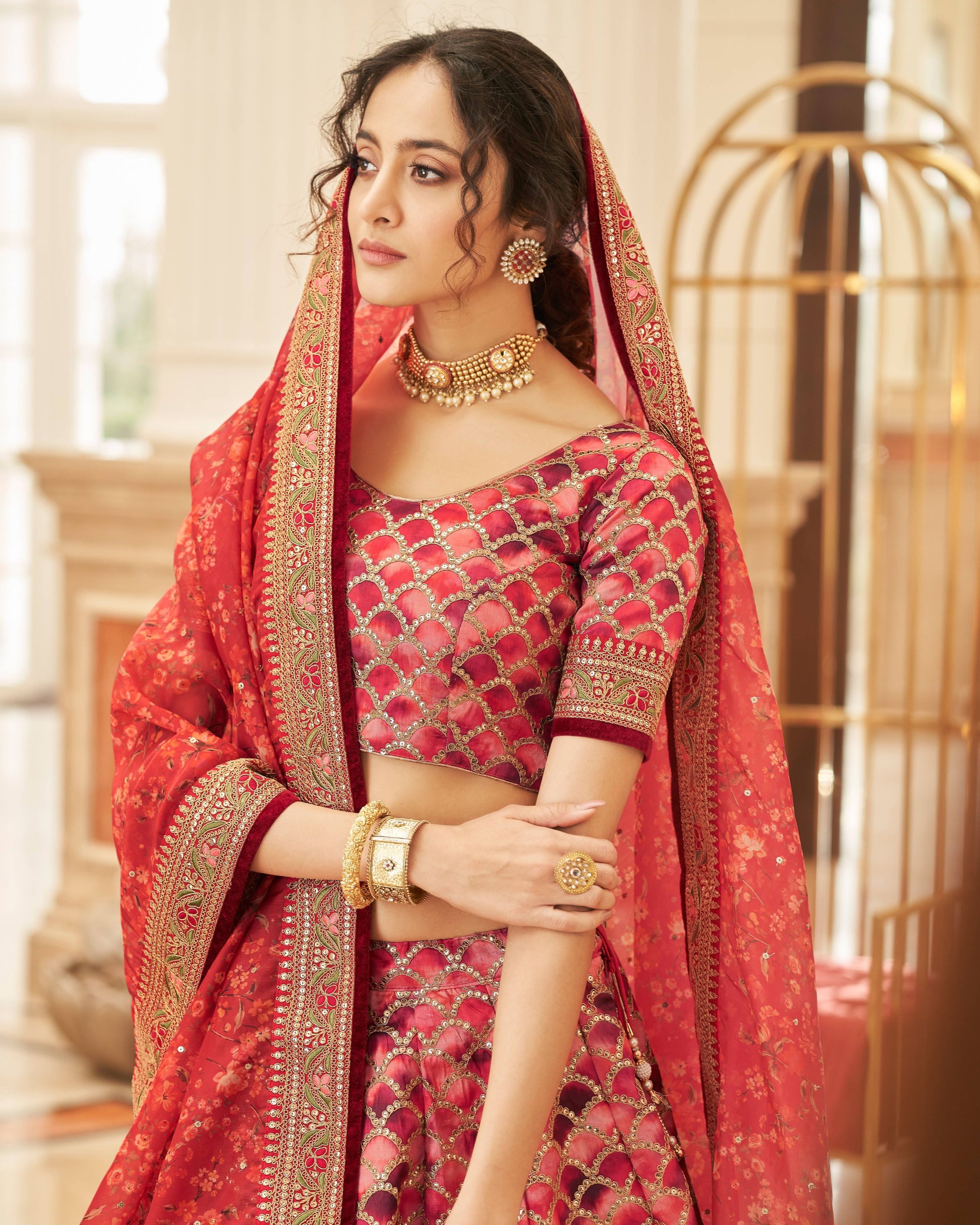 Woman in traditional red and gold outfit with jewelry in an elegant indoor setting
