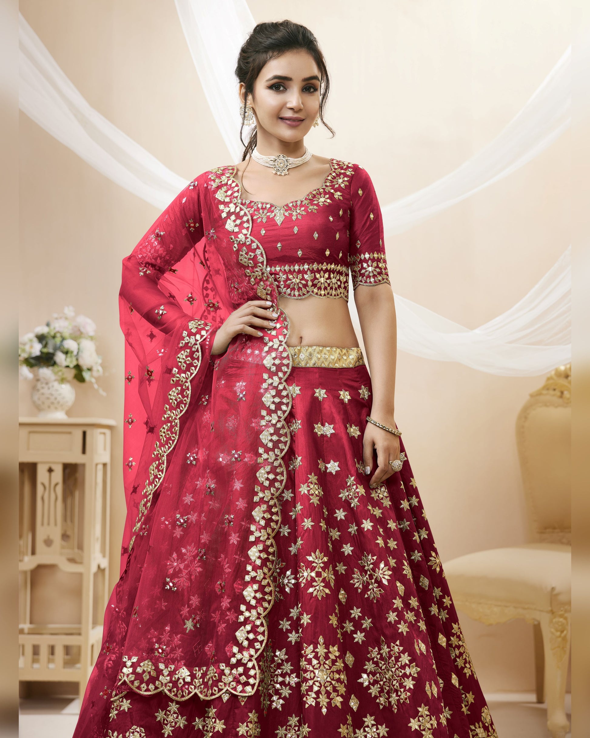 Woman wearing a red and gold embroidered traditional outfit in an elegant indoor setting.