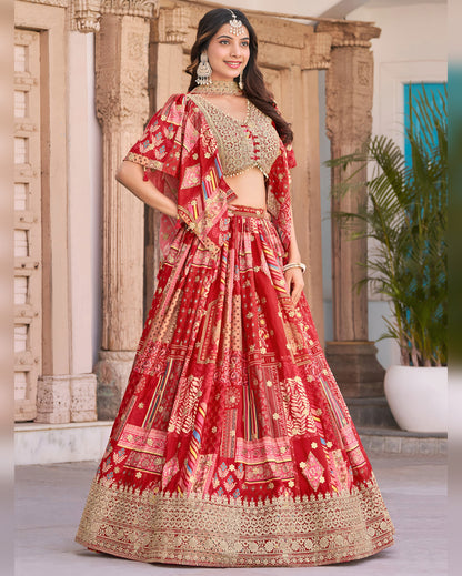 Woman in a red and gold traditional outfit standing indoors with decorative columns and plants.