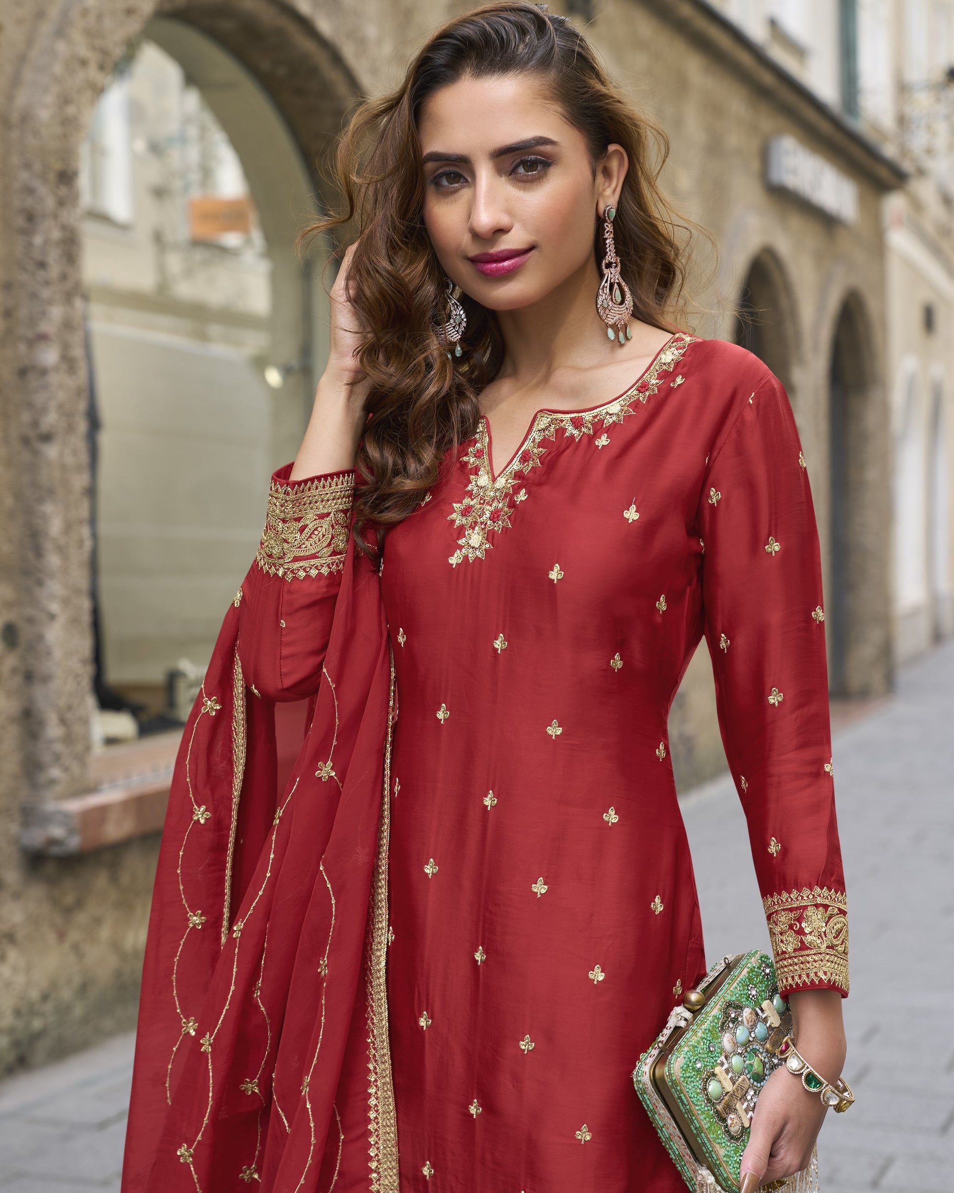 Woman in a red traditional outfit with gold embroidery standing outdoors.