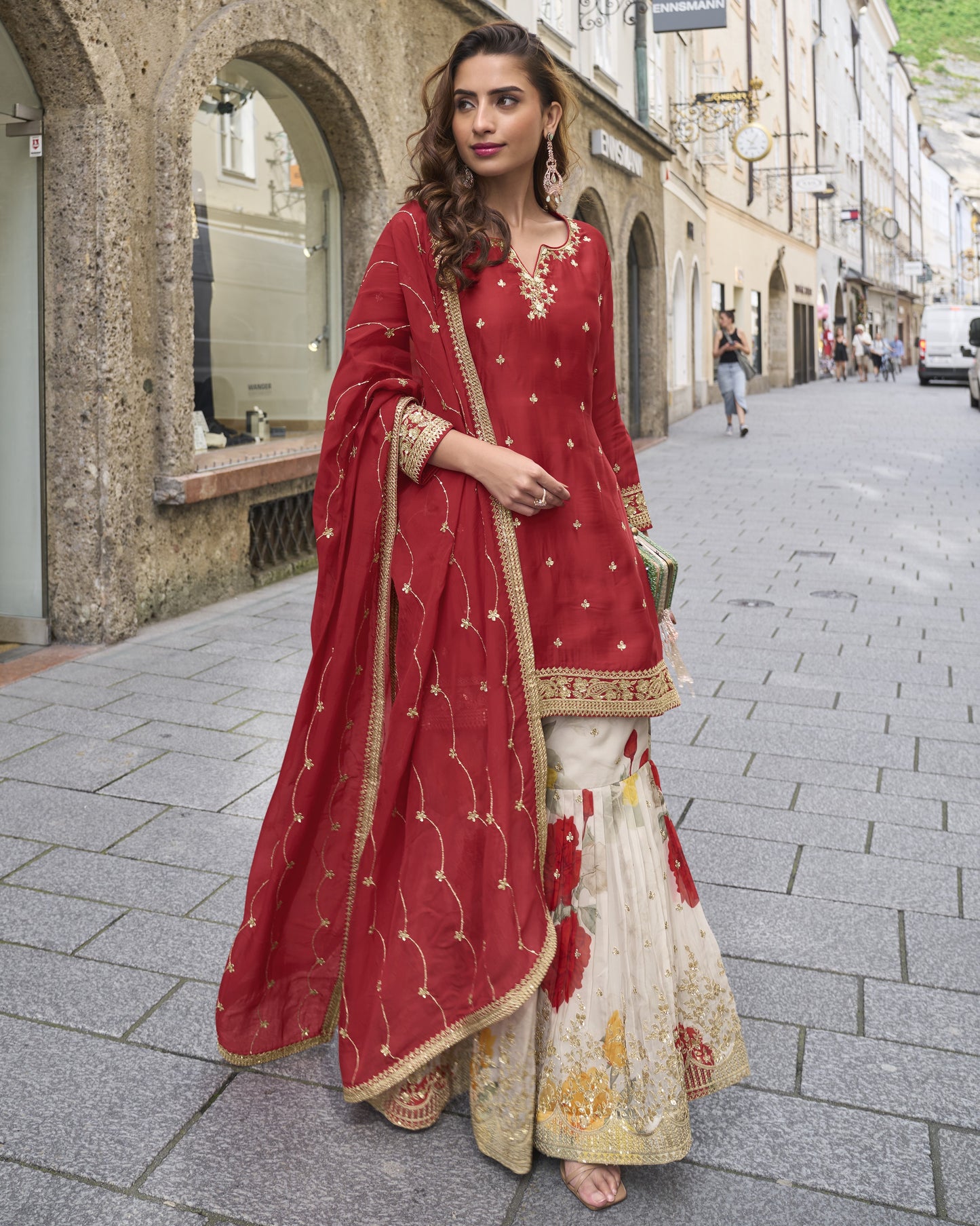 Woman in a red and gold traditional outfit walking on a street.