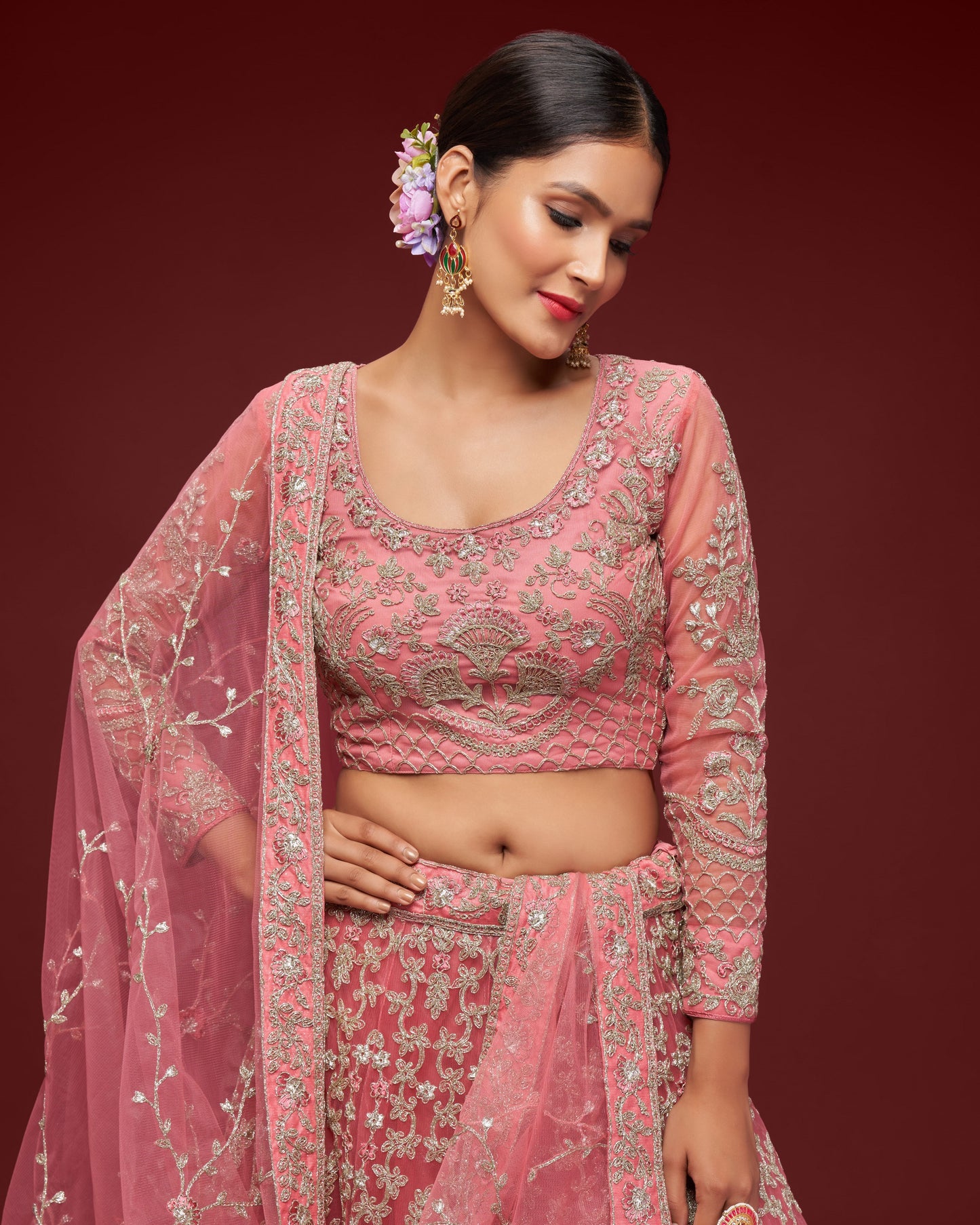 Woman wearing a pink embroidered traditional outfit with a matching dupatta against a dark red background