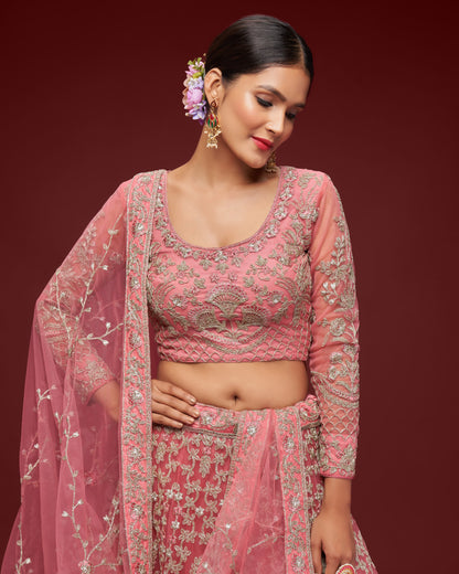 Woman wearing a pink embroidered traditional outfit with a matching dupatta against a dark red background