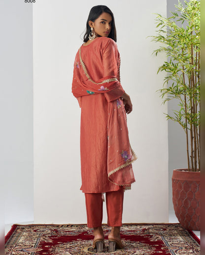 Woman in a peach-colored traditional outfit standing in a room with a plant and patterned rug.