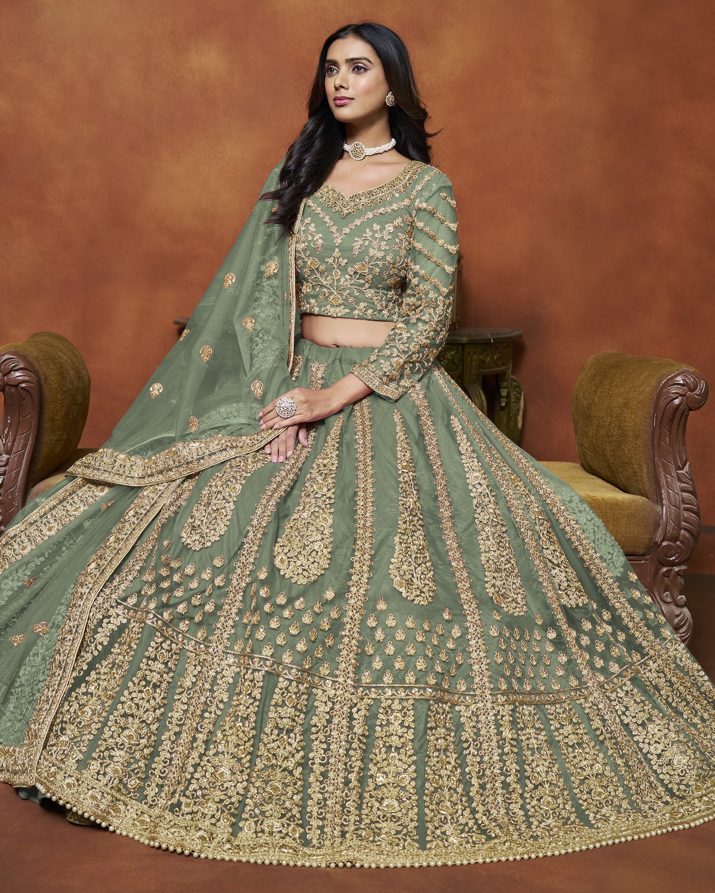 Woman in a green and gold embroidered traditional outfit sitting on a brown couch.