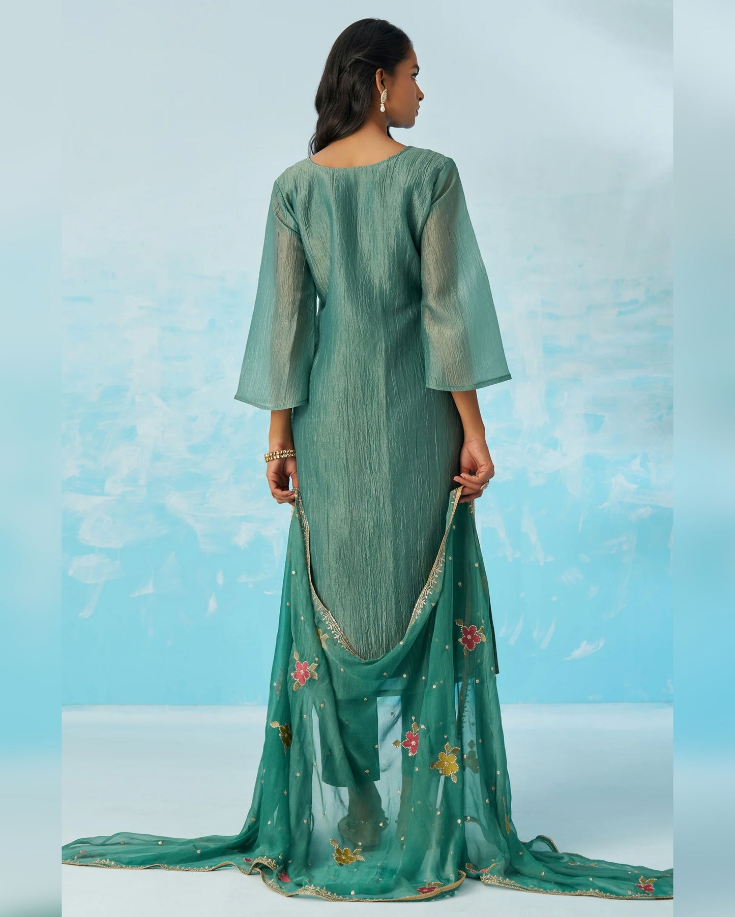 Woman wearing a green traditional outfit with a matching dupatta against a light blue background