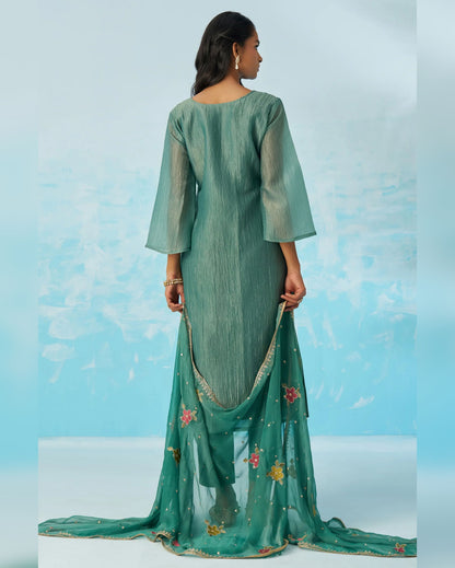 Woman wearing a green traditional outfit with a matching dupatta against a light blue background
