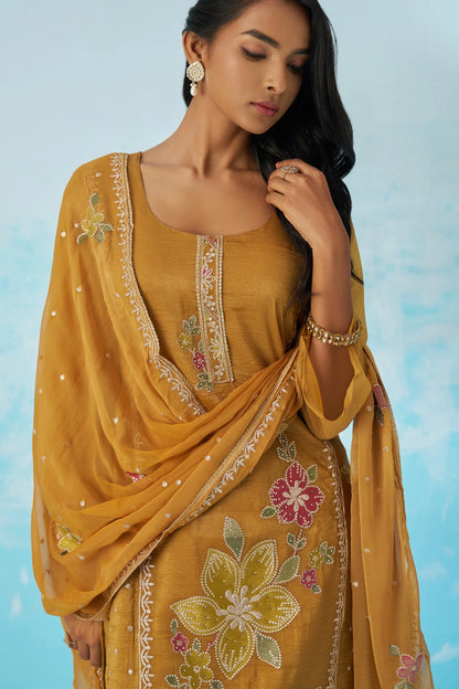 Woman wearing a mustard yellow embroidered saree against a light blue background