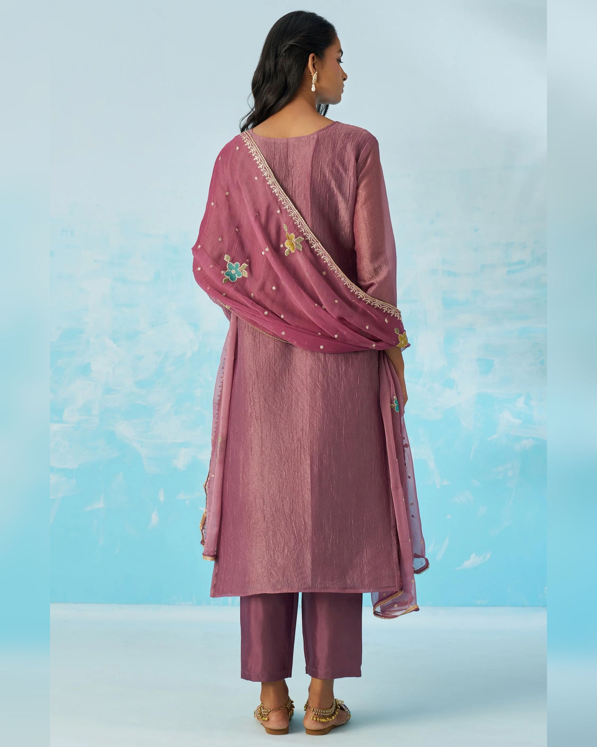 Woman wearing a pink traditional outfit with a matching dupatta against a light blue background