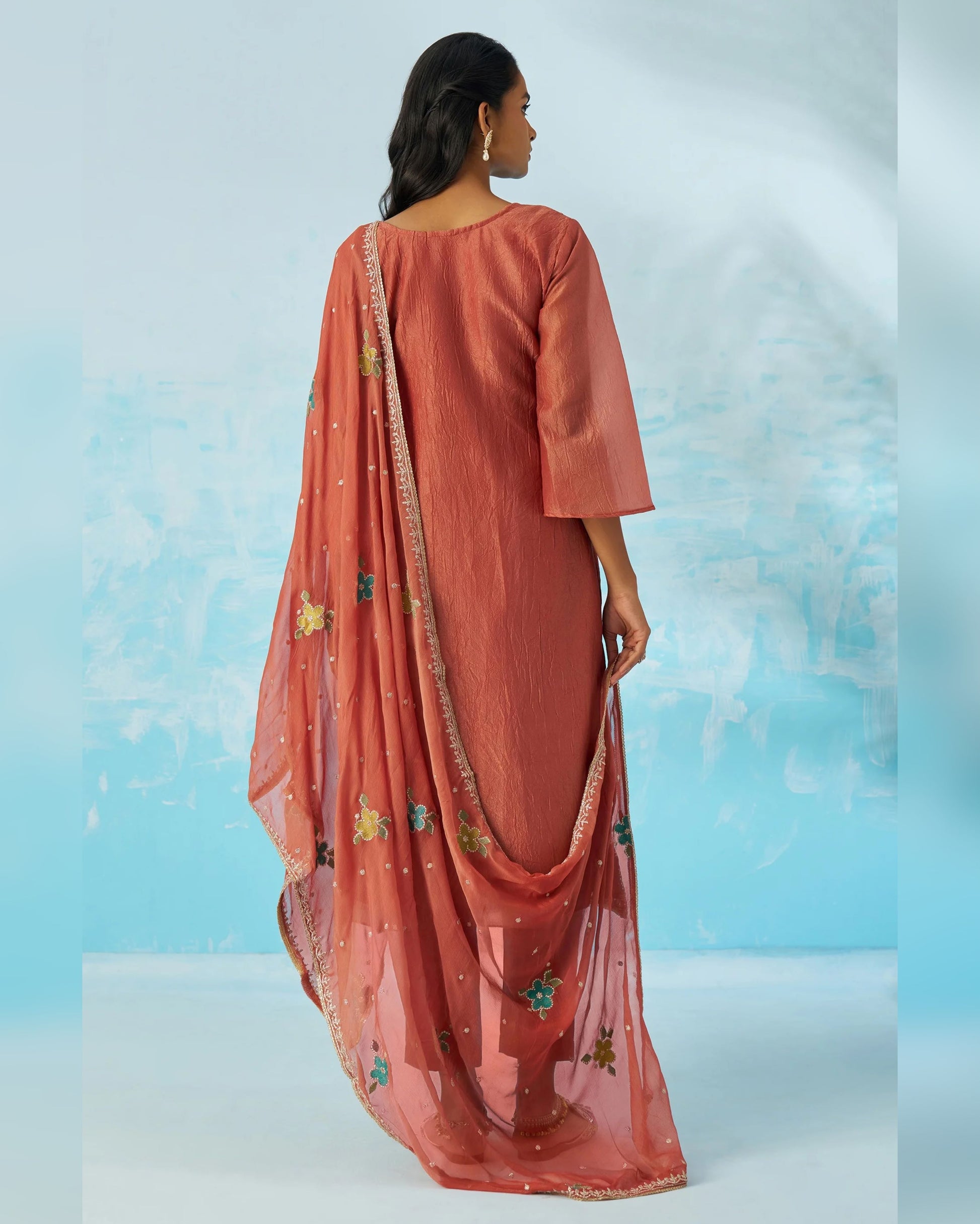 Woman wearing a peach-colored traditional outfit with a matching dupatta against a light blue background