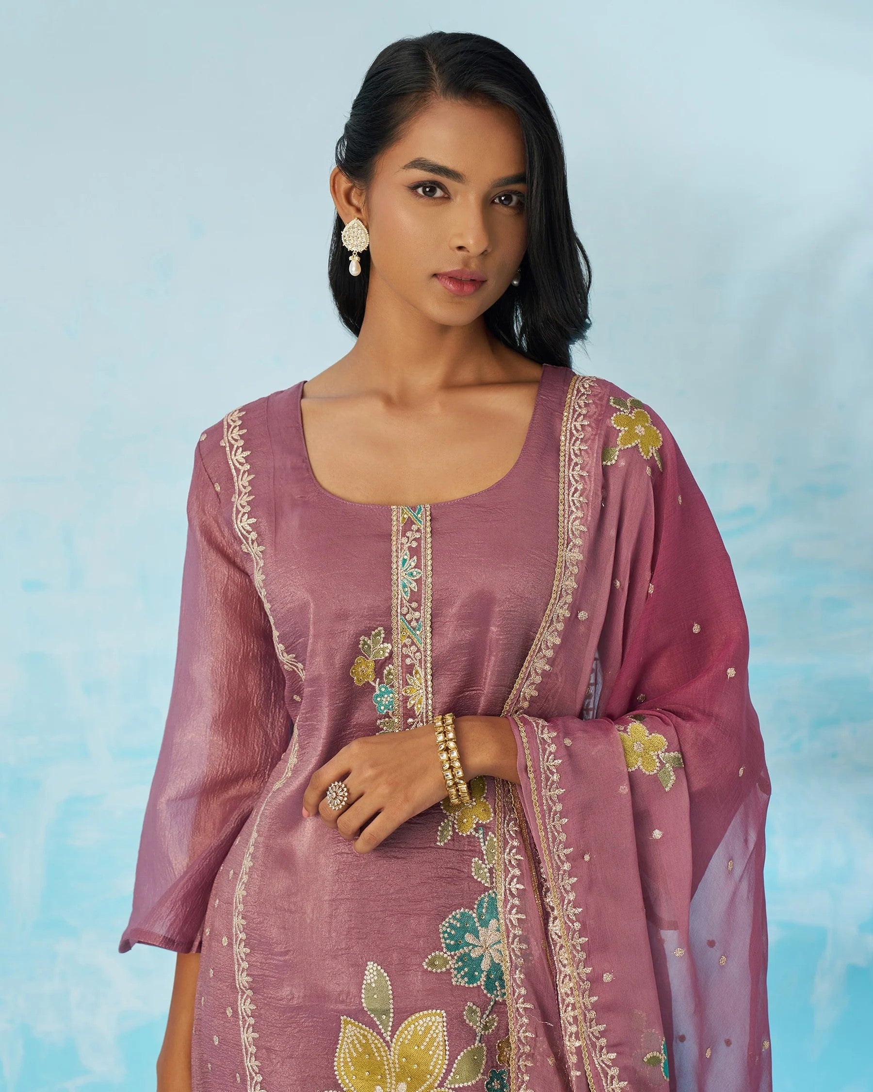 Woman wearing a pink embroidered traditional outfit against a light blue background