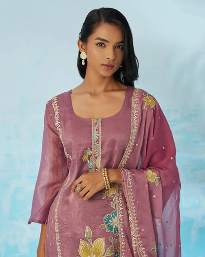 Woman wearing a pink embroidered traditional outfit against a light blue background