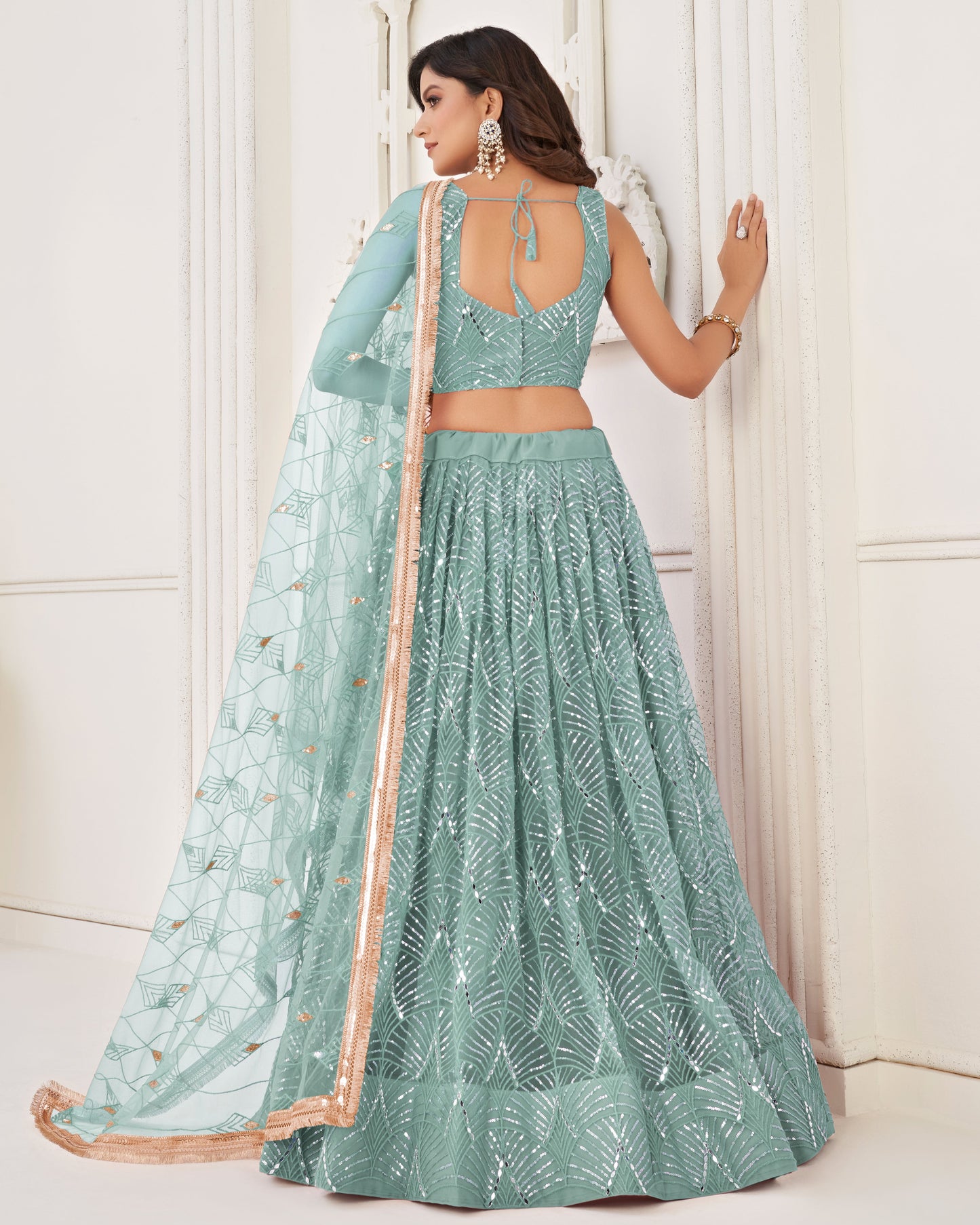 Woman wearing a light blue embroidered lehenga with a matching top against a white background