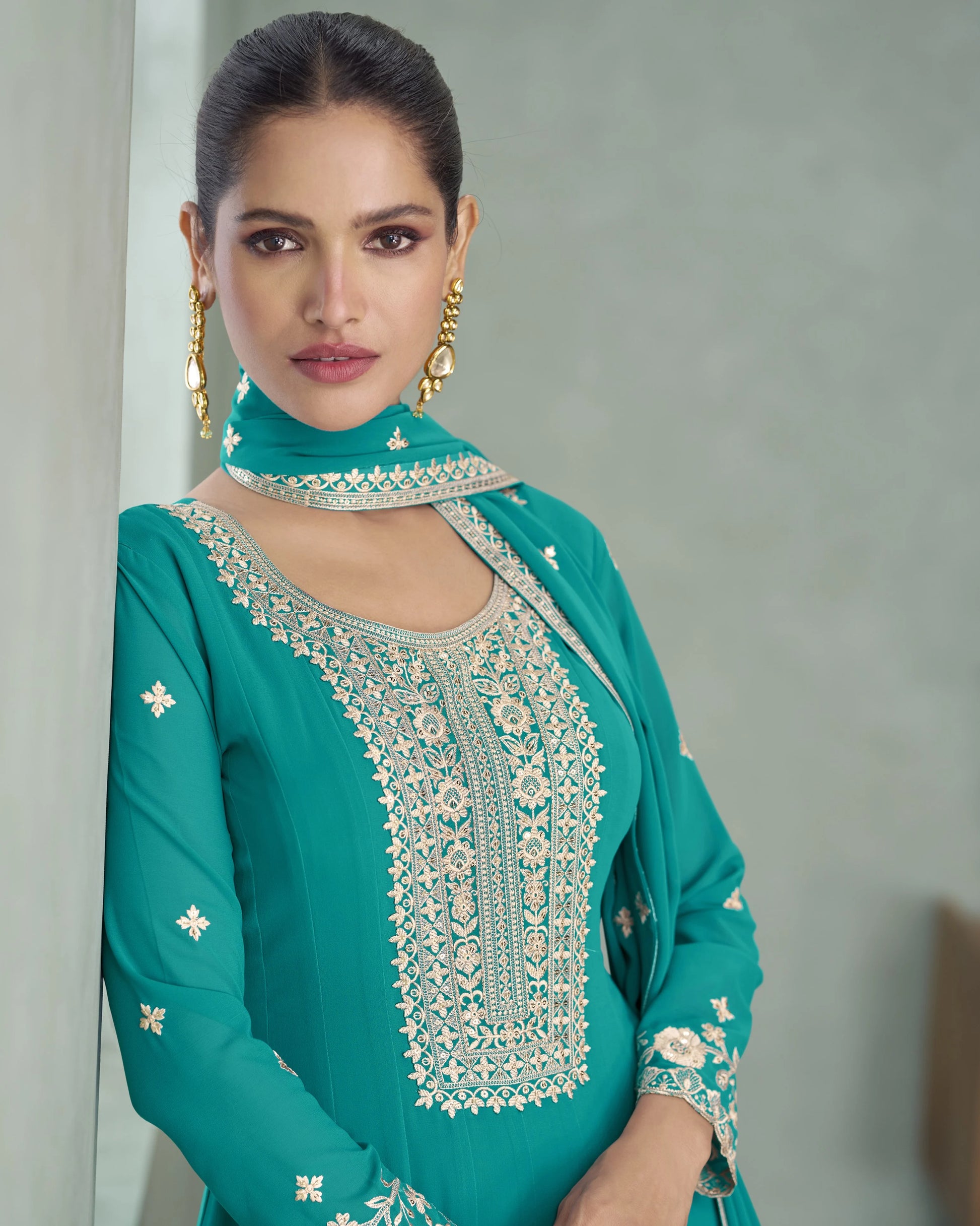 Woman wearing a teal embroidered outfit against a neutral background