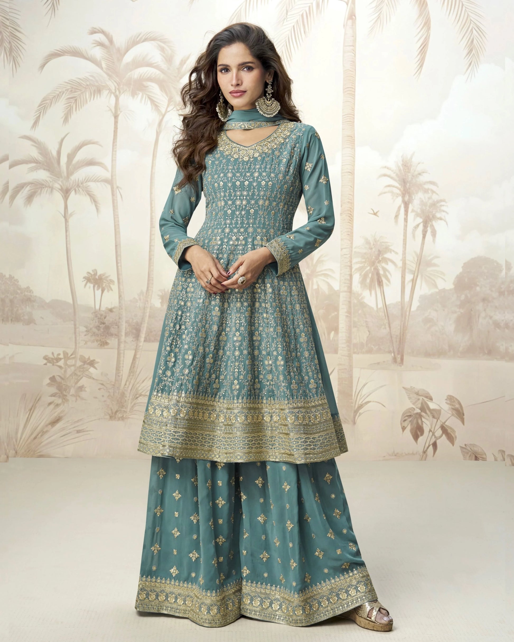 Woman wearing a teal traditional outfit with gold patterns against a decorative background