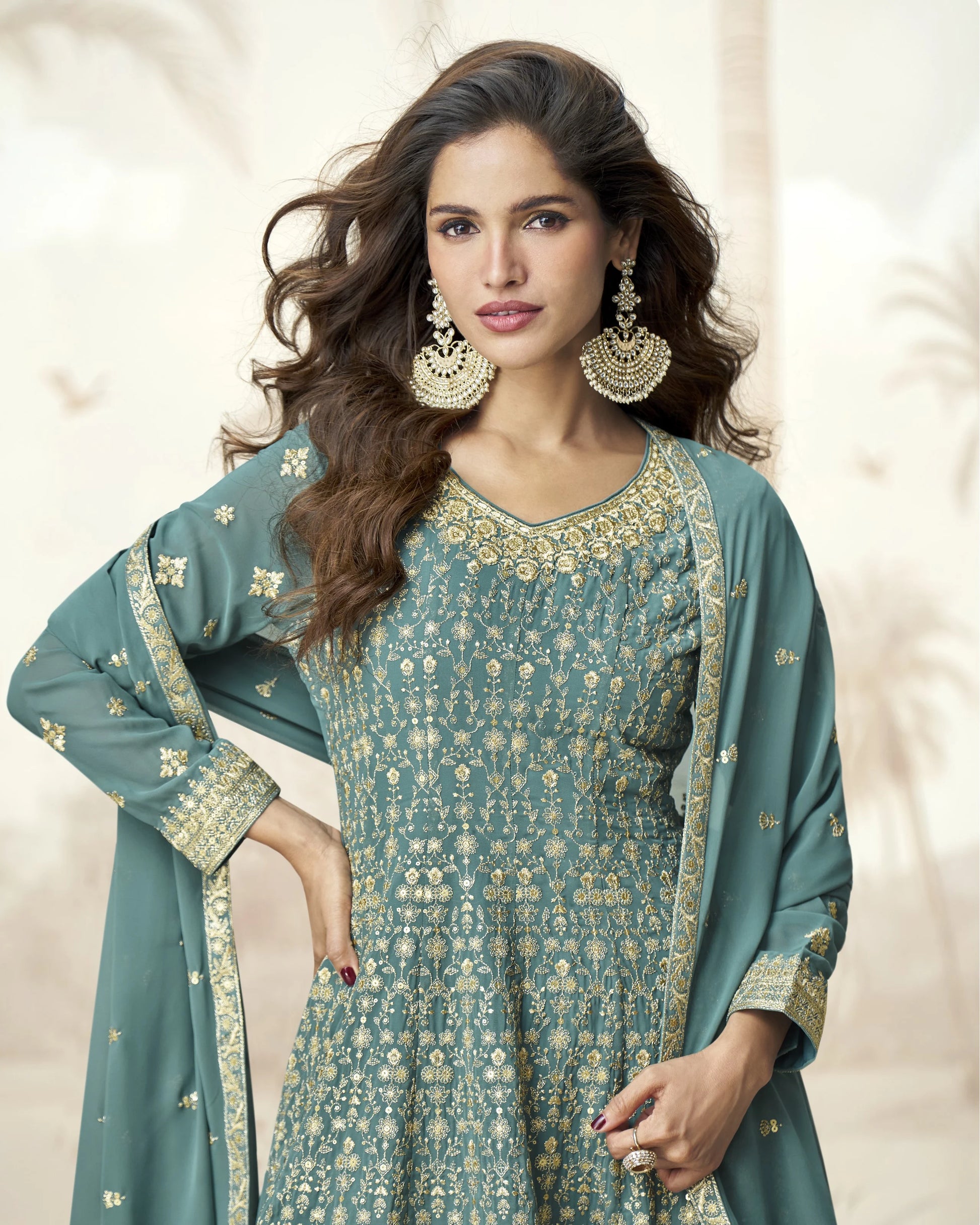 Woman wearing a teal traditional outfit with gold embroidery on a beige background